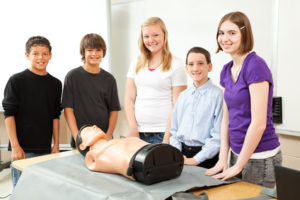 Group of teenagers with a CPR training dummy, about to learn cardiopulmonary resuscitation.